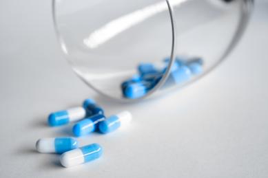 Blue antibiotic pills spilling from a glass cup